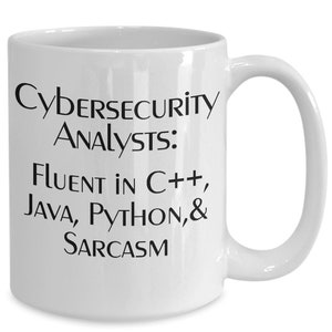Könnte beinhalten: Weiße Keramik-Kaffeetasse mit schwarzem Text, der "Cybersecurity Analysts: Fluent in C++, Java, Python, & Sarcasm" lautet.