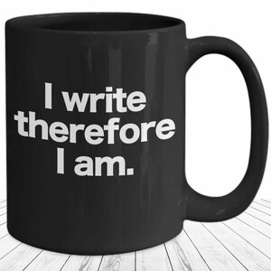 May include: Black coffee mug with white text that reads "I write therefore I am."