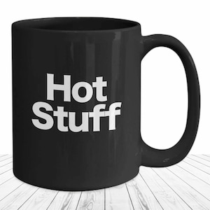 May include: Black ceramic coffee mug with white text that reads "Hot Stuff".
