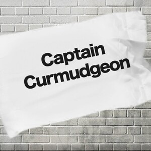 May include: A white piece of paper with the text "Captain Curmudgeon" written in black letters. The paper is crumpled and has a ripped edge.