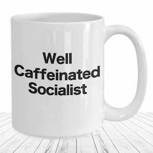 May include: White ceramic coffee mug with black text that reads "Well Caffeinated Socialist".