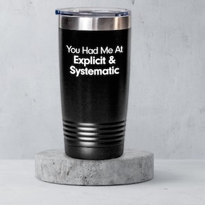 May include: Black stainless steel tumbler with a white inscription that reads "You Had Me At Explicit & Systematic".