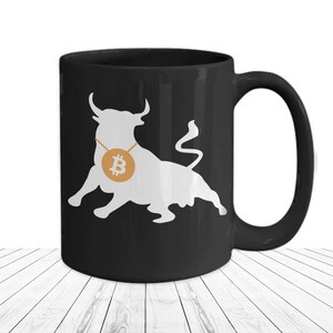 Könnte beinhalten: Schwarze Keramik-Kaffeetasse mit einer weißen Silhouette eines Bullen, der eine goldene Kette mit einem Bitcoin-Symbol trägt.