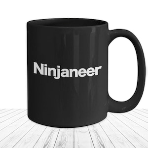 Könnte beinhalten: Schwarze Keramik-Kaffeetasse mit einer weißen Aufschrift "Ninjaneer".