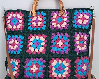 May include: A green crocheted tote bag with a bamboo handle and a brown shoulder strap. The bag is decorated with colorful squares.