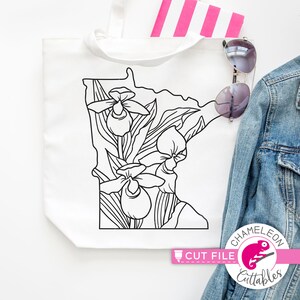 May include: A black and white line art design of the state of Minnesota with a floral pattern of lady slippers. The design is on a white tote bag. The text "CUT FILE" is in pink on a white background. The text "CHAMELEON CUTTABLES" is in pink on a white background with a chameleon graphic.