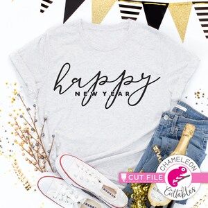 May include: A light gray t-shirt with the words "happy new year" in black script. The shirt is paired with blue jeans, white sneakers, and a champagne bottle. Gold and black party decorations are in the background.