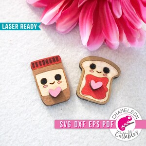 May include: Two laser-cut wooden ornaments, one shaped like a jar of peanut butter and the other like a slice of toast. Both have cute faces and a pink heart on them. The text "LASER READY" is visible in the top left corner. The text "SVG DXF EPS PDF" is visible in the bottom center of the image. The text "CHAMELEON CUTTABLES" is visible in the bottom right corner of the image.