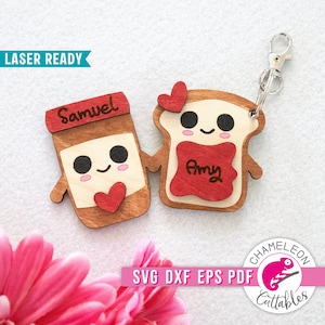 May include: A wooden keychain set featuring a peanut butter jar and a slice of toast, each with a smiling face and a heart. The peanut butter jar has the name "Samuel" and the toast has "Amy". The keychain is attached with a silver clasp.