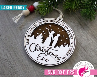 May include: A white wooden Christmas ornament with a brown wood background. The ornament features a silhouette of a couple standing in a snowy forest with stars in the sky. The text on the ornament reads "May you never be too grown up to search the skies on Christmas Eve".