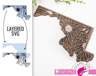 May include: A layered SVG cut file design of the state of Maryland with a floral pattern. The design is shown on a wooden cutout of the state. The text "LAYERED SVG" is visible on the design.