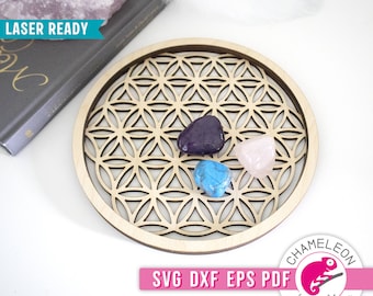 Puede incluir: Una bandeja de madera con un diseño de flor de la vida, perfecta para guardar cristales. La bandeja está cortada con láser y tiene un acabado de madera natural. La bandeja se muestra con cuatro cristales: una amatista morada, un cuarzo rosa, una turquesa azul y un cuarzo transparente.