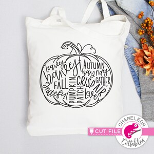 May include: A white canvas tote bag with a black pumpkin design filled with fall-themed words like "leaves," "harvest," and "autumn." The bag has two handles and a simple design, perfect for carrying groceries or other items. The bag also has the text "Cut File" and the logo of Chameleon Cuttables.