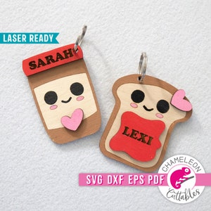 May include: Two laser-cut wooden keychains, one shaped like a jar of peanut butter with the name "SARAH" on the lid and a pink heart, and the other shaped like a slice of bread with the name "LEXI" on the red jelly and a pink heart.