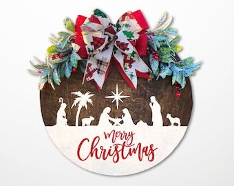 May include: A round wooden Christmas ornament with a white background and a red "Merry Christmas" inscription. The ornament features a silhouette of the nativity scene with a palm tree, a star, and a red and white bow with green accents.