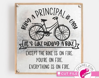 Puede incluir: Un letrero cuadrado con fondo de metal plateado y marco de madera. El letrero presenta una ilustración de bicicleta negra y el texto "Ser director es fácil. Es como andar en bicicleta, excepto que la bicicleta está en llamas. Estás en llamas. Todo está en llamas."