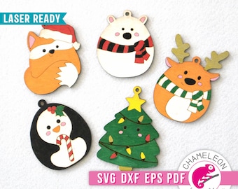 May include: A collection of five wooden Christmas ornaments. The ornaments include a fox in a Santa hat, a polar bear with a scarf, a reindeer with a scarf, a penguin with a candy cane, and a Christmas tree. The ornaments are laser-ready and feature the text "SVG DXF EPS PDF".