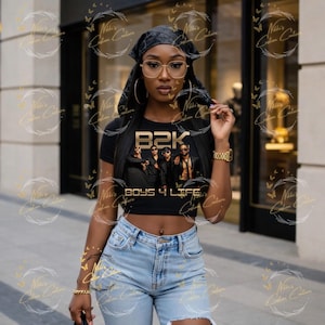 May include: Black crop top featuring the text "B2K BOYS 4 LIFE" with a graphic of four men. The top is paired with light wash denim shorts. The image also includes gold-framed glasses and a black headscarf.