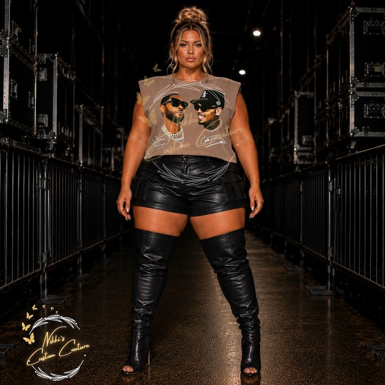 May include: A woman wearing a sleeveless brown t-shirt with a graphic of two men, black leather shorts, and black thigh-high boots. The boots have open toes and high heels. The background is dark with stage equipment.