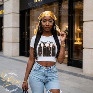 Puede incluir: Una camiseta corta blanca con el texto "Jagged Edge" y un gráfico del grupo musical. La modelo lleva un pañuelo amarillo estampado, pendientes de aro grandes y vaqueros rotos de color azul claro.