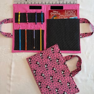 Pu&ograve; includere: Una custodia in tessuto rosa per libri da colorare con motivo a pois bianchi, dotata di tasche interne per matite e un libro da colorare. La custodia misura circa 43 cm di larghezza. Una seconda custodia piegata con stampa Minnie &egrave; in primo piano.
