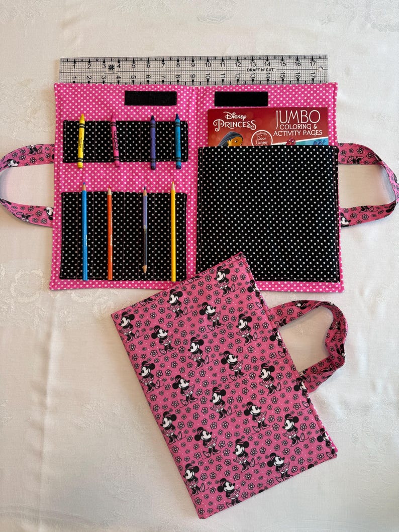 Pu&ograve; includere: Una custodia in tessuto rosa per libri da colorare con motivo a pois bianchi, dotata di tasche interne per matite e un libro da colorare. La custodia misura circa 43 cm di larghezza. Una seconda custodia piegata con stampa Minnie &egrave; in primo piano.