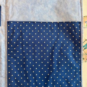 May include: A light blue fabric organizer featuring a large, dark blue rectangular pocket with a white polka dot pattern. The organizer includes a rectangular hook-and-loop fastener strip at the top and a smaller vertical pocket on the left side.