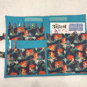 May include: A fabric activity organizer featuring a teal background with white polka dots and a dark blue pattern of Ariel the mermaid. It includes pockets holding crayons and markers, and a Disney Stitch Jumbo Coloring and Activity Book.
