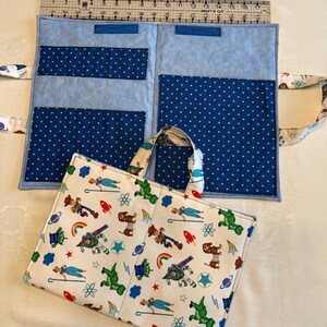 May include: A fabric organizer with a white exterior featuring a colorful cartoon character print and a light blue interior with dark blue polka-dot pockets. A metal ruler placed along the top edge shows the item measures 17 inches in width.