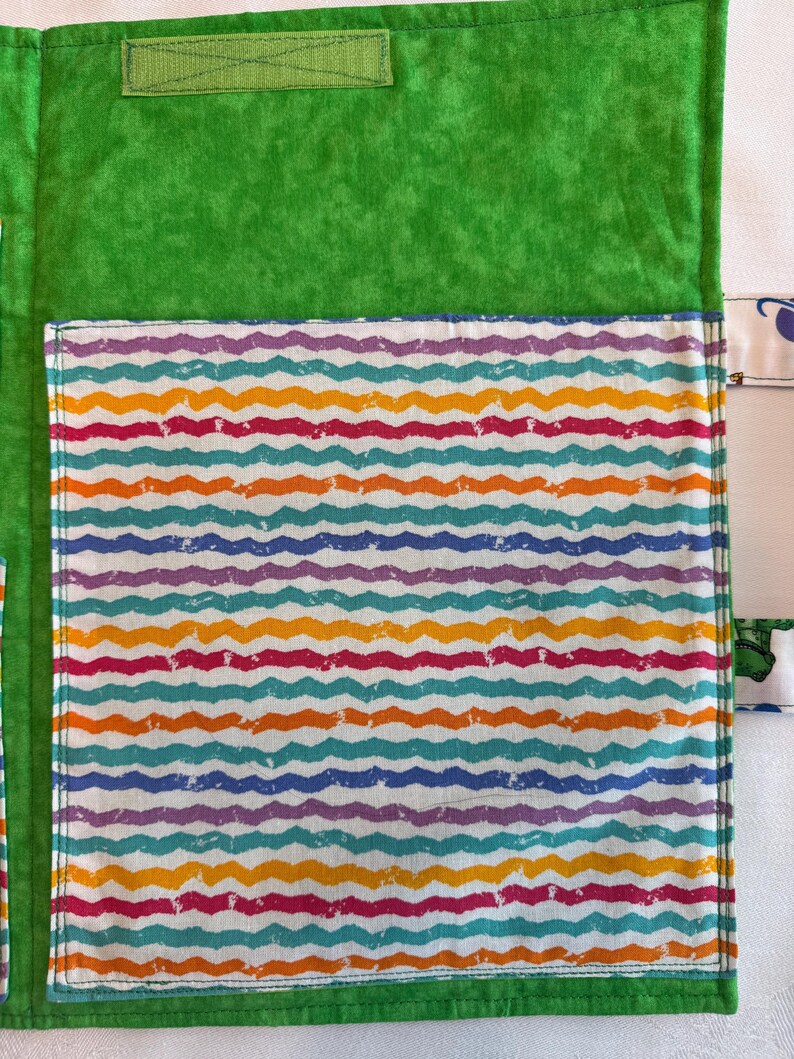May include: A bright green fabric organizer featuring a large rectangular pocket with a repeating pattern of horizontal wavy lines in shades of purple, orange, teal, and pink. The organizer includes a green hook-and-loop fastener strip at the top.