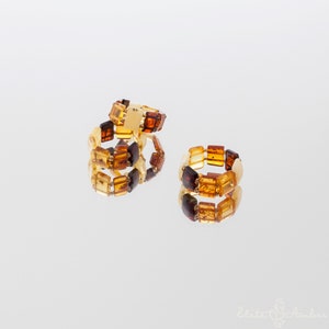 Puede incluir: Tres anillos de &aacute;mbar con cuentas cuadradas en tonos marr&oacute;n, amarillo y naranja. Los anillos est&aacute;n apilados uno encima del otro.