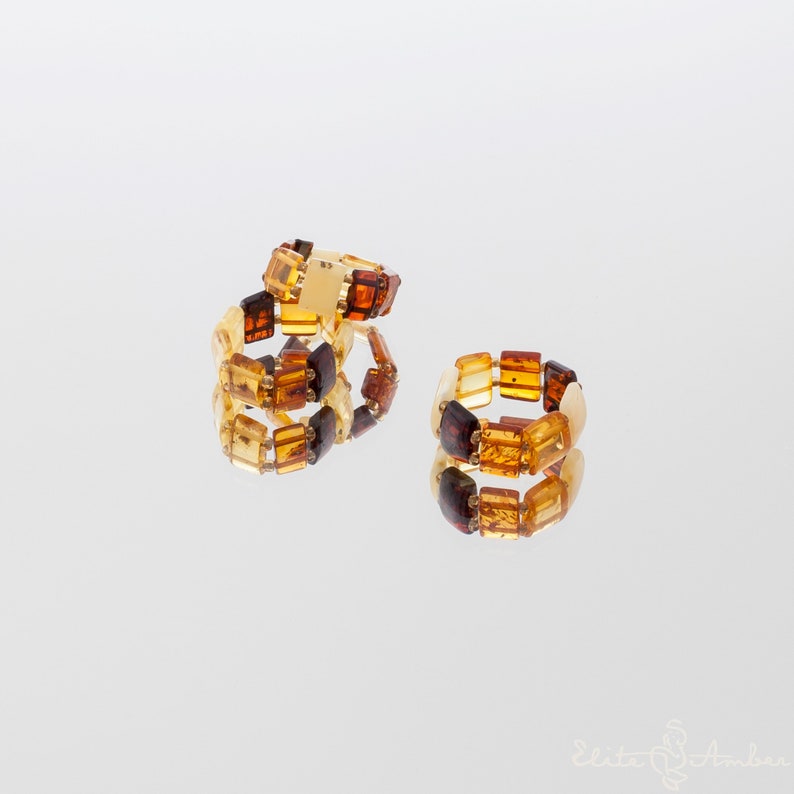 Puede incluir: Tres anillos de &aacute;mbar con cuentas cuadradas en tonos marr&oacute;n, amarillo y naranja. Los anillos est&aacute;n apilados uno encima del otro.
