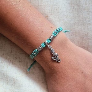 Puede incluir: Una pulsera de macramé turquesa con cuentas plateadas y un pequeño dije de pulpo. La pulsera está hecha a mano y presenta un diseño trenzado. El dije es detallado y agrega un toque náutico al accesorio.
