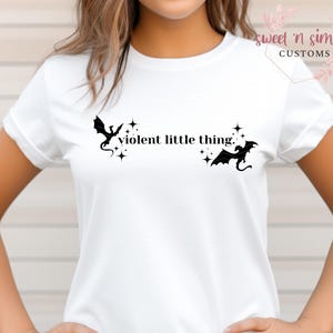 May include: White t-shirt with a black silhouette of two dragons and the text "violent little thing."
