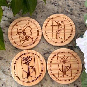 May include: Four round wooden coasters with a light brown finish. Each coaster features a unique, etched design within a circle, with a dotted border. The designs appear to be abstract line art. The coasters are arranged on a speckled surface.