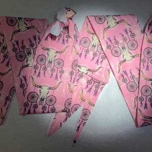 May include: Three pink fabric headbands with a white trim and a pattern of purple dreamcatchers and cow skulls.
