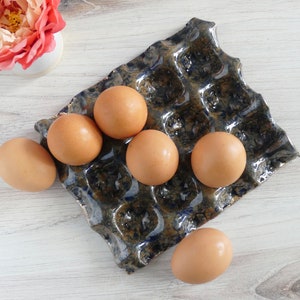 May include: A blue and brown ceramic egg holder with six brown eggs inside. The holder is shaped like a traditional egg carton.