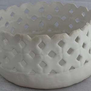 May include: White ceramic bowl with a decorative lattice design. The bowl has a round shape and a smooth, white finish.