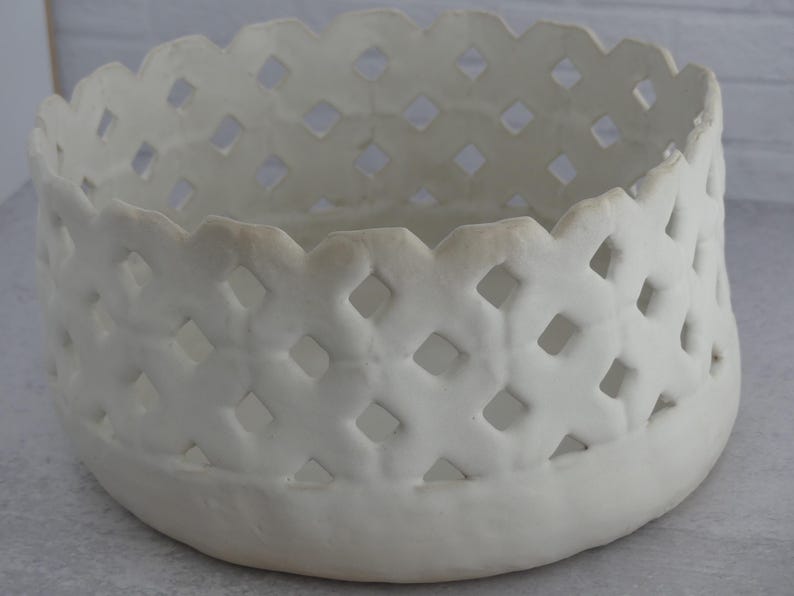 May include: White ceramic bowl with a decorative lattice design. The bowl has a round shape and a smooth, white finish.