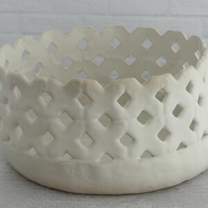 May include: White ceramic bowl with a woven pattern. The bowl has a wide, open top and a rounded bottom.