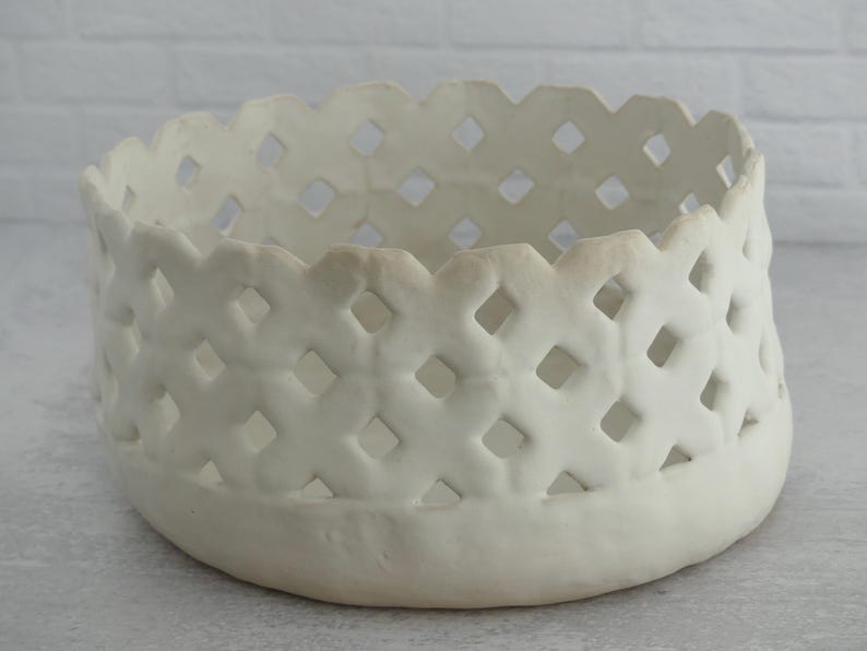 May include: White ceramic bowl with a woven pattern. The bowl has a wide, open top and a rounded bottom.