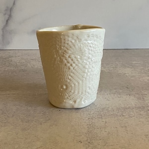 Può includere: Tazza in ceramica bianca con un motivo a pizzo in rilievo.