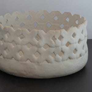 May include: White ceramic bowl with a decorative, openwork design. The bowl has a round shape and a raised rim.