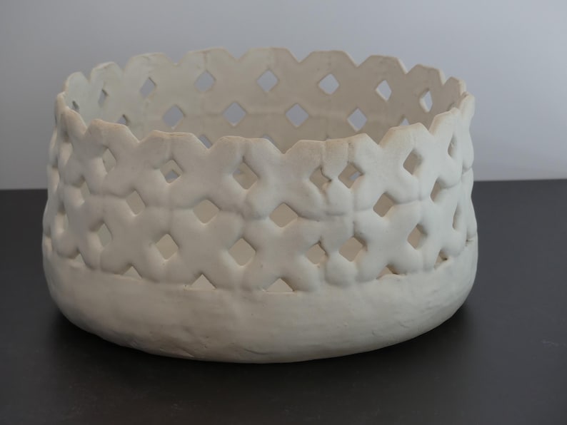 May include: White ceramic bowl with a decorative, openwork design. The bowl has a round shape and a raised rim.