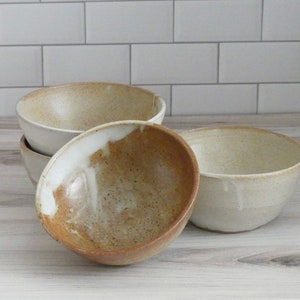 May include: Four ceramic bowls in various shades of brown and white. The bowls are stacked on top of each other, with the largest bowl on the bottom and the smallest bowl on top.
