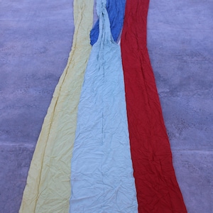 Puede incluir: Tiras de tela coloridas en amarillo, azul claro, azul oscuro, blanco y rojo. La tela parece arrugada, con cada color formando una franja vertical. El fondo es una superficie gris.