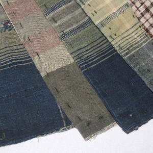 May include: A collection of six fabric scraps in various shades of blue, green, brown, and beige. The fabric scraps are woven with a plaid pattern and have been sewn together.