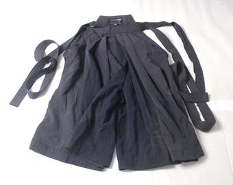 May include: Dark grey hakama trousers with wide legs and attached waist ties. The traditional Japanese garment is made of a soft, flowing fabric. The trousers are laid out on a white surface.