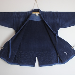 May include: A dark blue indigo-dyed Japanese martial arts uniform, or "Judogi", with a diamond pattern stitched into the fabric. The uniform is hanging on a wooden dowel rod with a chain attached to each side.