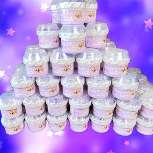 Może przedstawiać: Piramida małych, przezroczystych plastikowych pojemników wypełnionych fioletowym slime. Każdy pojemnik ma białą pokrywkę i etykietę z napisem "Purplestars02 SLIME". Tło to fioletowy gradient z białymi gwiazdami.